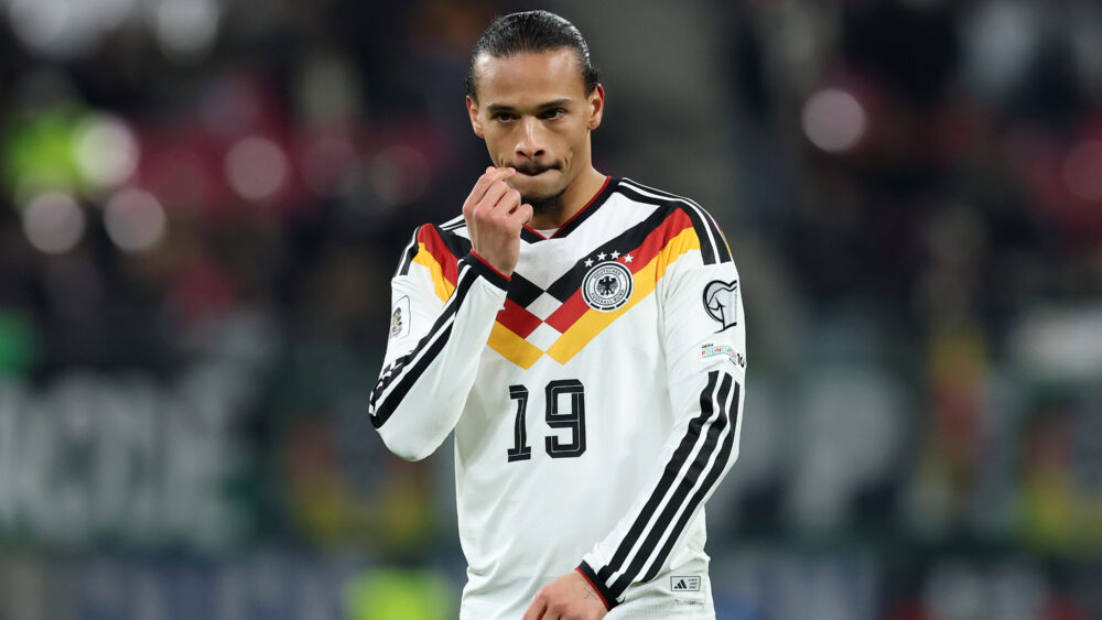 Leroy Sané im Trikot des DFB-Teams. Er hat eine Hand im Gesicht.