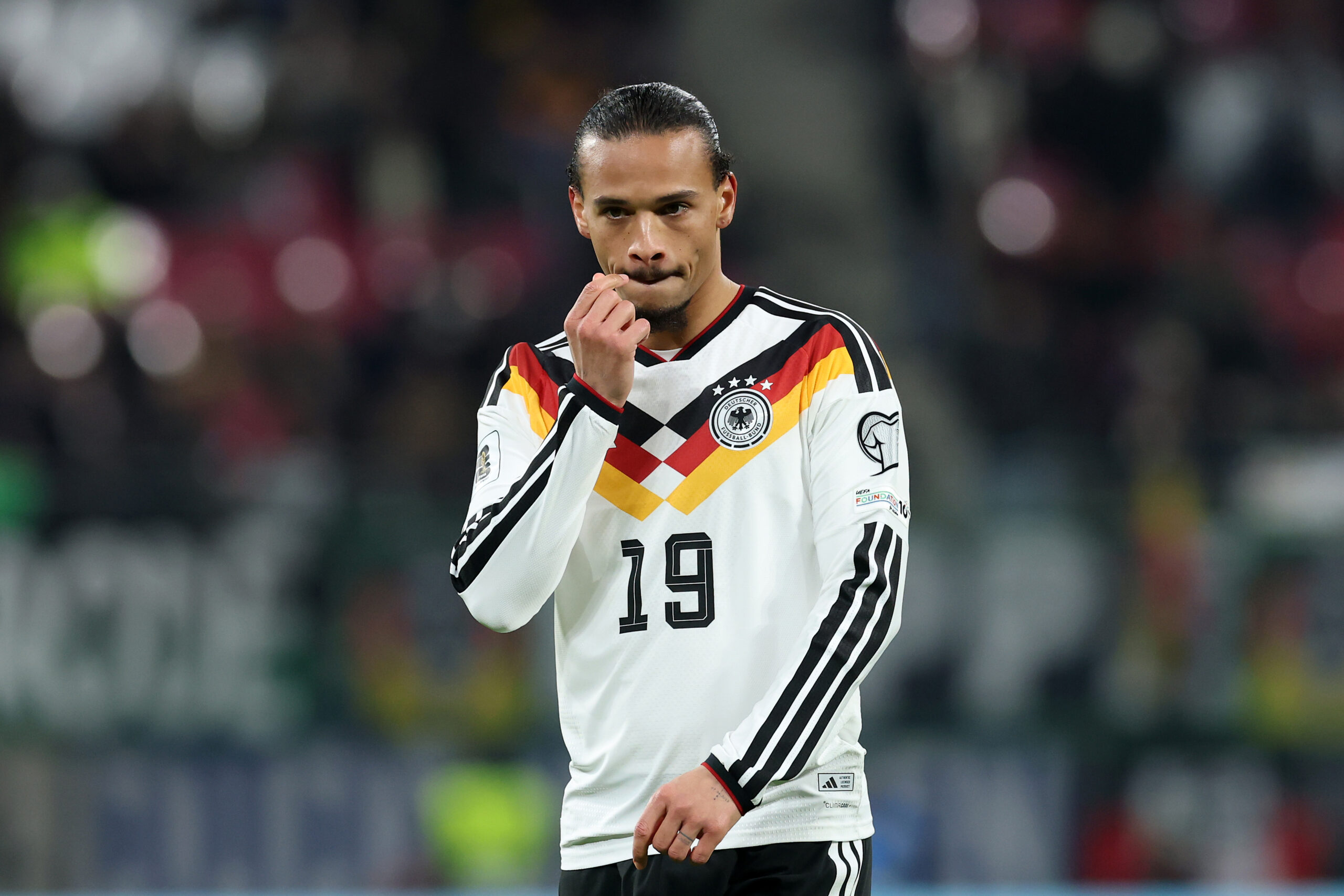 Leroy Sané im Trikot des DFB-Teams. Er hat eine Hand im Gesicht.