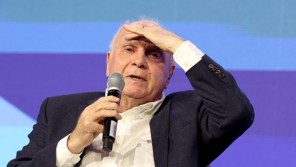 Uli Hoeneß vom FC Bayern hält in der einen Hand ein Mikrofon, die andere ist auf seinem Kopf.