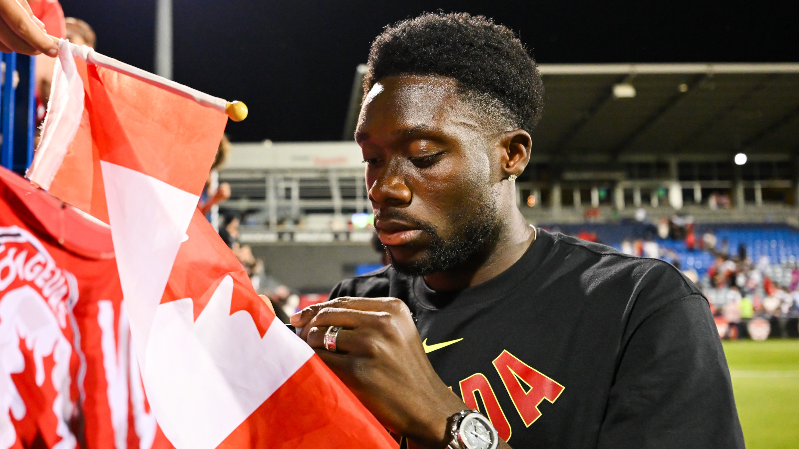Alphonso Davies unterschreibt bei der WM 2026 eine Fahne von Kanada.