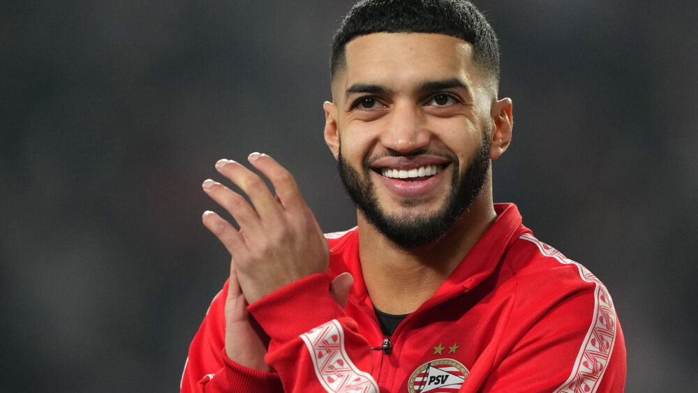 Ismael Saibari (bald FC Bayern) mit einem breiten Grinsen, er hält die Hände in der Nähe des Gesichts.